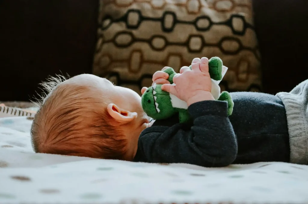 In the picture, a baby on a bed holding a plush in his hands.