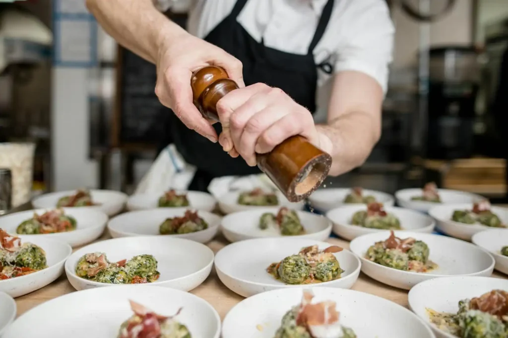 In the picture, a close-up on the hands of a chef putting salt on some plates ready to be served to guests.