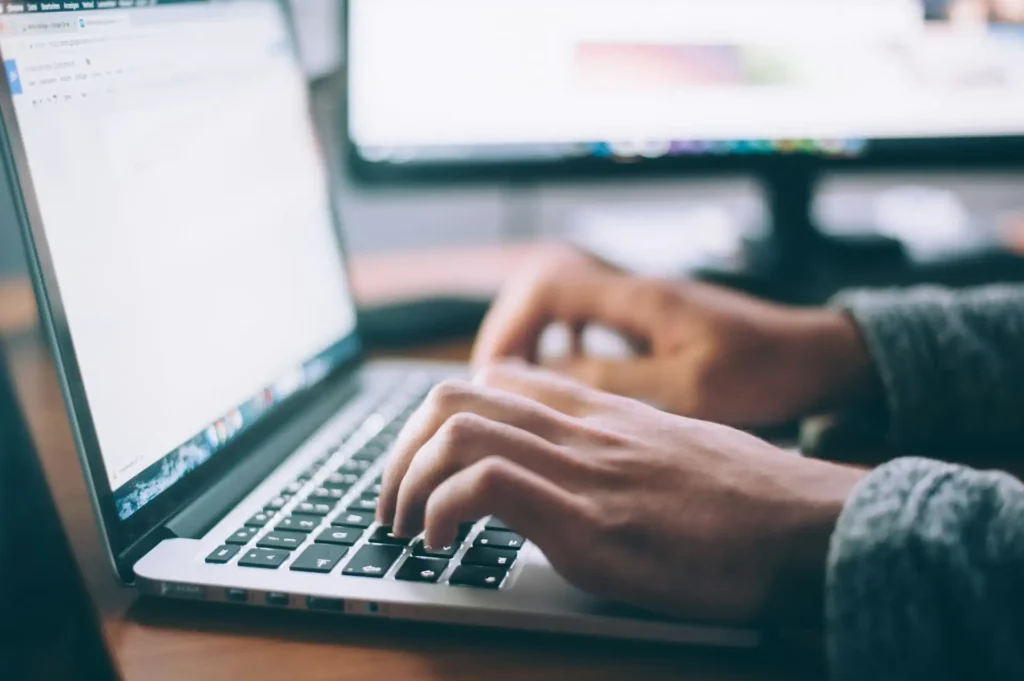 In the picture, a close-up on the hands of a person working on a laptop.